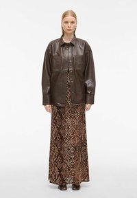 Veste en cuir marron avec deux poches poitrine, portée sur une robe maxi à imprimé serpent dans des tons de marron et de beige. Texture lisse.