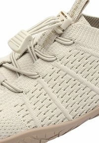 Scarpa da corsa di un beige chiaro con tomaia in maglia testurizzata, lacci elasticizzati e una suola in gomma resistente con battistrada a motivo.