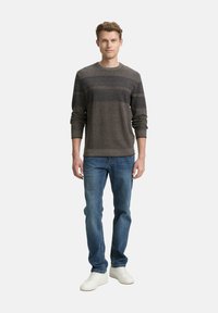 Grijze trui met horizontale donkere strepen, gecombineerd met blauwe denim jeans en witte sneakers. Casual fit, ronde halslijn, gebreide textuur.