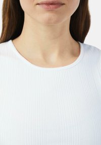 Biały top z prążkowanej tkaniny i okrągłym dekoltem. Materiał ma gładką teksturę i delikatny połysk, podkreślając pionowe linie na całej powierzchni.