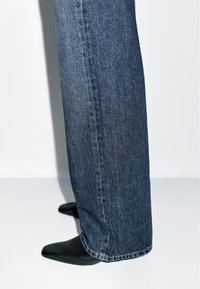 Wide-leg denim jeans in dark blue with a matte finish. Close to the ankle, worn with pointed black heels. Clean lines and minimal detailing.