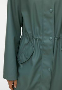 Giacca impermeabile verde con coulisse in vita, chiusure a bottoni a pressione e tasche a patta sul davanti. Tessuto liscio e maniche lunghe.