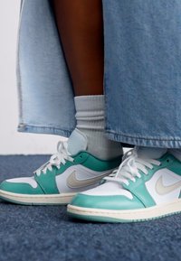Turkis og hvite Nike-sneakers med en teksturert overflate, som har en gull swoosh og hvite lisser. Brukt med hvite ankelstrømper og et denimskjørt.