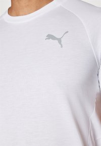 Valge lühikeste varrukatega spordipoolt särg, mis on valmistatud pehmest kangast, ja mille vasakus ülanurgas on helehall Puma logo.