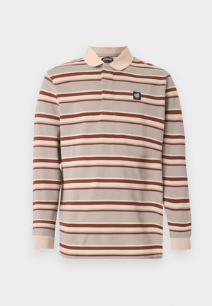 Hosszú ujjú galléros póló bézs, barna és krémszínű vízszintes csíkokkal, bézs színű gallérral és mandzsettákkal, valamint egy kis fekete logó folttal a mellkasán.