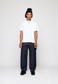 Hvid bomulds t-shirt, afslappet pasform, parret med mørkeblå løse denimbukser. Sort strikket beanie og sorte sko fuldender looket.
