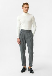 Witte coltrui gecombineerd met grijs gestreepte broek met voorplooien en zijknopen. Zwarte loafers maken de look af.