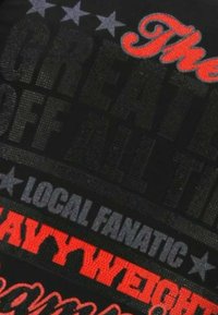 Zwart T-shirt met dikke tekst in verschillende stijlen: "The GREATEST", "LOCAL FANATIC" en "HEAVYWEIGHT" in rood en grijs.