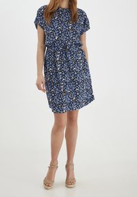 Námořnické květinové šaty s krátkými rukávy, nařaseným pasem a detailem na zavázání. Vyznačují se malými modrými a zelenými květy na tmavém pozadí.