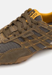 Brown suede and mesh shoe featuring gray accents, yellow stitching, and a rubber sole. Includes brand logo on the tongue.