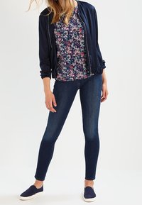 Námořnická bombarďák přes květinový top, spárovaný s tmavě modrými skinny džíny a námořnickými slip-on botami. Hladká tkanina s elastickými akcenty.