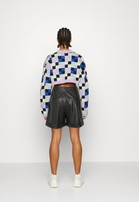 Pull court avec un motif à carreaux multicolores, mettant en avant le violet, le bleu et le vert. Associé à un short en cuir noir.