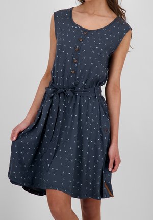 Robe sans manches bleu marine avec un petit motif d'oiseaux blancs, patte de boutonnage devant, ceinture nouée à la taille et poche latérale avec détail en forme de cœur.
