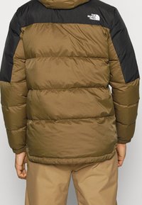 Puffjacka i olivgrön med svarta axlar, med ett quiltat mönster, logotypdetalj och elastiska muddar, som erbjuder värme och komfort.