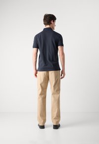 Marineblå polo skjorte med korte ærmer, parret med beige chinos. Stofdetaljerne ser glatte ud, med en lige pasform og minimal dekoration.