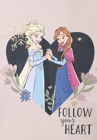 Ilustracja dwóch postaci trzymających się za ręce w kształcie serca, otoczonych kwiatami. Tło w delikatnym beżu z napisem "PODĄŻAJ ZA SWOIM SERCEM."