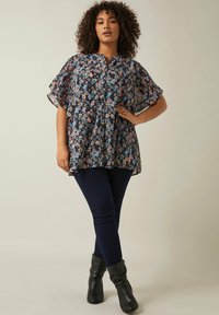 Bluse mit floralem Muster und kurzen, gerafften Ärmeln in Marineblau, mit pinken und blauen Blumen. Kombiniert mit dunklen Jeans und schwarzen Ankle-Boots.