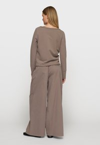 Haut marron à manches longues avec un col large, associé à un pantalon marron ample. Le tissu semble doux avec une texture lisse.