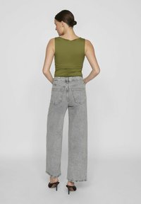 Canottiera verde oliva aderente, abbinata a jeans a gamba larga grigi chiari con vita media e due tasche posteriori. Tacchi neri completano il look.