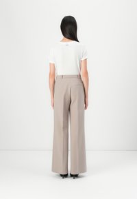 Maglietta bianca con maniche arrotolate e un piccolo logo sul retro, abbinata a pantaloni beige a vita alta e a gamba larga. Tacchi a spillo neri.