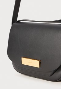 Borsa a tracolla nera in pelle con una texture liscia, caratterizzata da un accento hardware rettangolare in tonalità oro sulla patta. Include una tracolla regolabile.