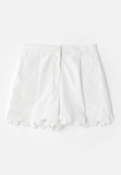 White shorts featuring a textured embroidered design along the sides and scalloped hem. Smooth fabric with decorative bead accents.
