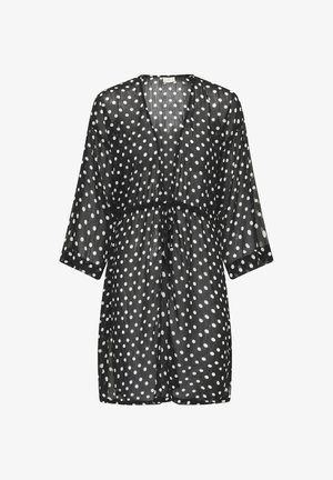 Robe noire transparente longueur genou avec des pois blancs, manches trois-quarts et ceinture à nouer devant.
