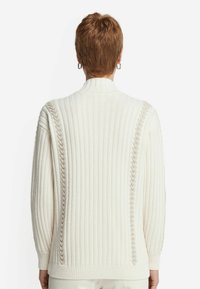 Hvid ribstrikket sweater med høj hals, strukturerede kabelstrik-detaljer ved skuldrene og tætsiddende manchetter. Blødt, strikket stof.