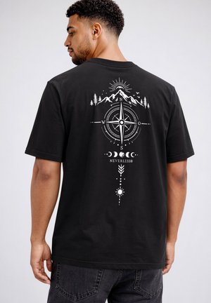 Man wearing black t-shirt with white compass, mountain, trees, moon phases, and sun graphic centered on the back.