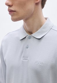 Ανοιχτό γκρι πόλο μπλούζα με υφή υφάσματος, τρίκοντη λωρίδα με κουμπιά και διακριτικό λογότυπο BOSS κεντημένο στο στήθος.