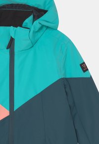 Tyrkysová a tmavě modrá bunda s růžovým akcentem, vybavená vysokým límcem, kapucí a zapínáním na zip. Materiál vypadá hladce a lehce.