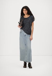 Black leopard-print short-sleeve top, light wash denim maxi skirt, brown ankle boots with buckles, holding a dark handbag.