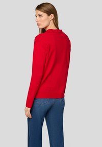 Roter Pullover mit Rundhalsausschnitt, gerippter Textur und langen Ärmeln, kombiniert mit blauen Jeans im klassischen 5-Taschen-Design.
