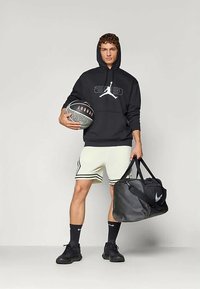 Melnā kapuca ar grafiku, baltie šorti ar melnām svītrām, melni sporta apavi, basketbola bumba un melna sporta soma. Gludas tekstūras un sportisks dizains.