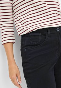 Jean en denim foncé avec une coupe slim et de subtils détails de couture, associé à une chemise à manches longues rayée en crème et bordeaux.