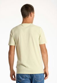 Camiseta amarilla claro de manga corta con cuello redondo, que presenta una textura suave y un dobladillo recto, combinada con jeans azules.