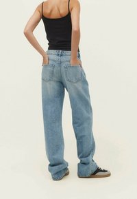 Jeans ampi in denim blu chiaro con vita alta e due tasche posteriori, abbinati a un top aderente nero e sneaker nere.