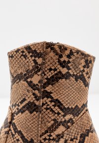 Snake-pattern ankle boot with a tan and black color scheme. Made of textured material, featuring a structured design and visible stitching.