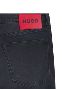 Tumma farkkujen musta nahkainen takatasku, jossa näkyy punainen "HUGO"-merkki ja kauniit ompelukoristeet.