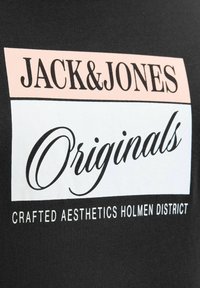 Μαύρο ύφασμα με το λογότυπο Jack & Jones Originals σε ροζ και λευκά ορθογώνια, το κείμενο λέει Crafted Aesthetics Holmen District.
