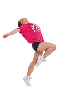 Rosa oversized t-shirt med vit text, svarta shorts och vita högskurna sneakers; dynamisk pose med ett ben lyft och armarna utsträckta.