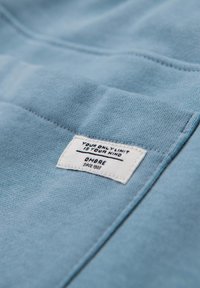Una tela azul clara con una textura suave presenta una etiqueta blanca que dice: "TU ÚNICO LÍMITE ES TU MENTE", "OMBRE" y "DESDE 1986".