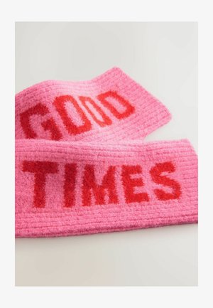 Rozā filca galvas josla ar uzrakstu "LABAS LAIKES" un "LAIKES" spilgti sarkanos burtos. Tekstūra rada mīkstu, pūkainu izskatu ar izcilām burtiem.