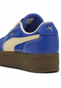 Baskets Puma bleu et beige avec semelle marron texturée, logo Puma doré au talon et sur le côté, et doublure intérieure blanche.