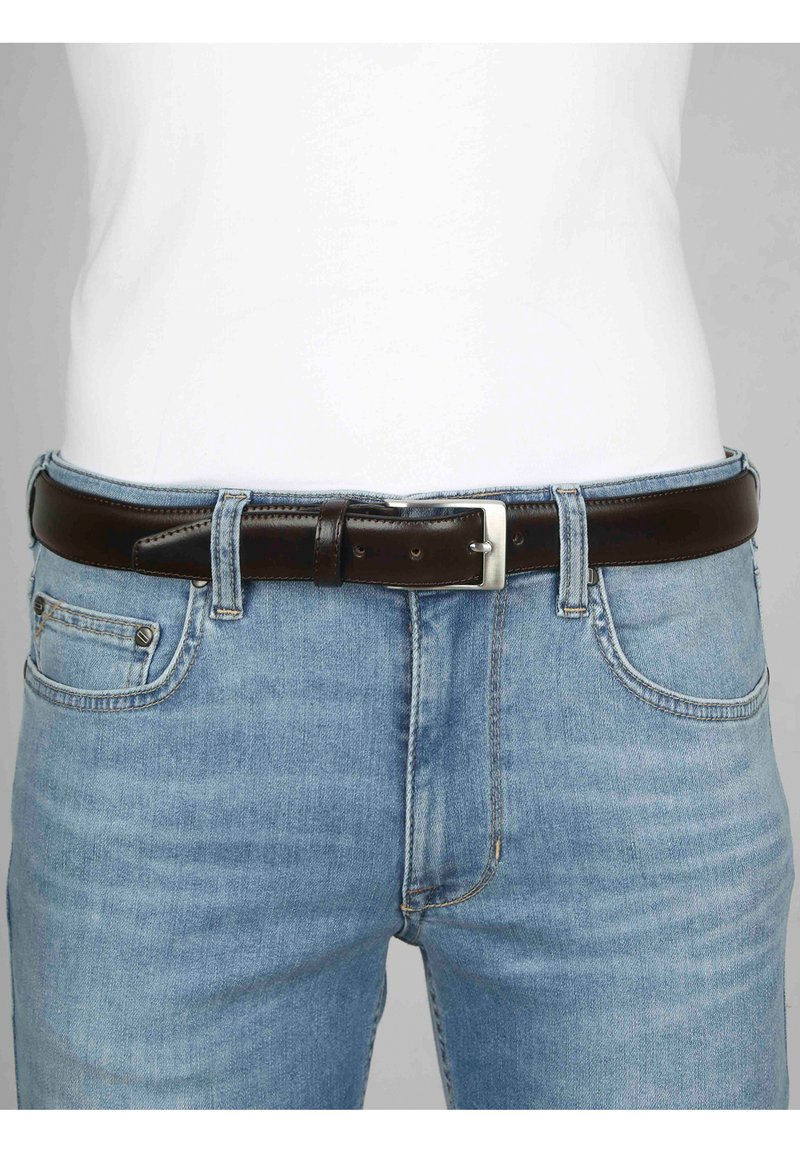 Bruine leren riem met een zilveren metalen gesp, gedragen over lichtblauwe denim jeans. De riem heeft een gladde textuur en verschillende gaatjes voor aanpassing.
