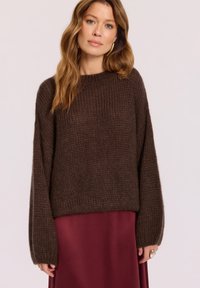 Ciemnobrązowy sweter dzianinowy o luźnym kroju, z szerokimi rękawami i okrągłym dekoltem, w połączeniu z bordową satynową spódnicą.