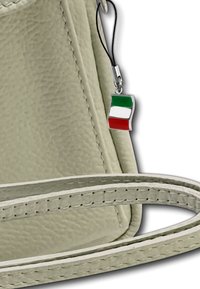 Lichtbeige leren tas met een gestructureerd oppervlak, voorzien van een zilveren bedel in de vorm van de Italiaanse vlag en een platte, smalle strap.