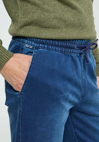 Pantalons bleu marine avec une taille élastique, un cordon de serrage ajustable et des poches latérales. Le tissu semble lisse avec un léger éclat.