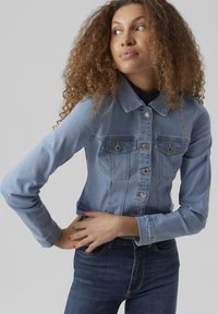 Svjetloplava traper jakna s gumbom sprijeda, dva džepa na prsima i dugim rukavima s prilagođenim dizajnom. Glatka tekstura s suptilnim šavovima.