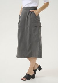 Gonna midi grigia con vita elastica, dotata di due tasche laterali e una superficie liscia. Abbinata a mules neri con tacco a blocco.